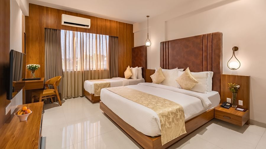 A hotel room features a comfortable king-size bed and a smaller single bed, along with a desk and a mounted television - Lords Eco Inn Ambaji.