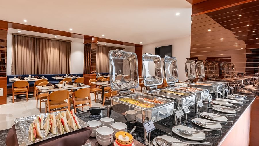 A buffet spread with covered food warmers, plates, and other serving dishes is ready in a dining area - Lords Eco Inn Ambaji.