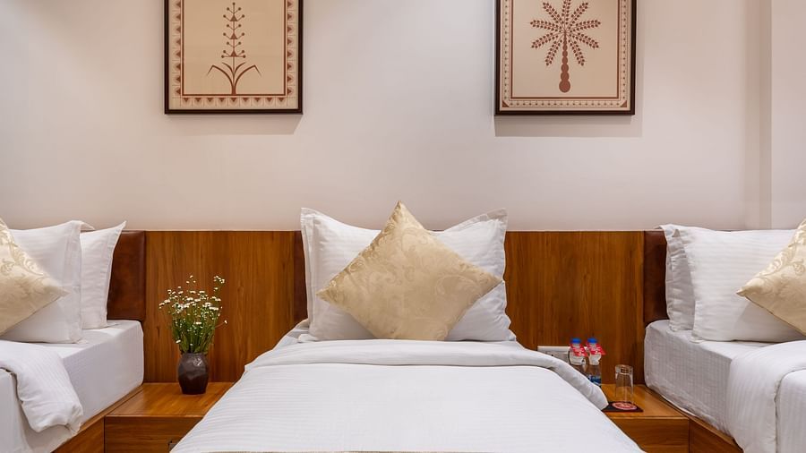 Three single beds with white linens and decorative pillows are positioned under framed botanical prints on a wall - Lords Eco Inn Ambaji.