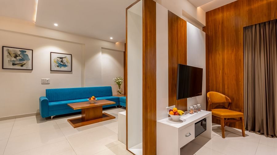 A hotel living area includes a sofa, a wooden coffee table, a mounted television, and a cushioned chair - Lords Eco Inn Ambaji.