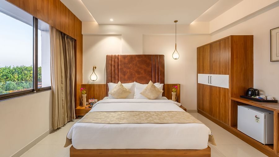 A comfortable bed is the central feature of a hotel room with a large window and storage furniture - Lords Eco Inn Ambaji.