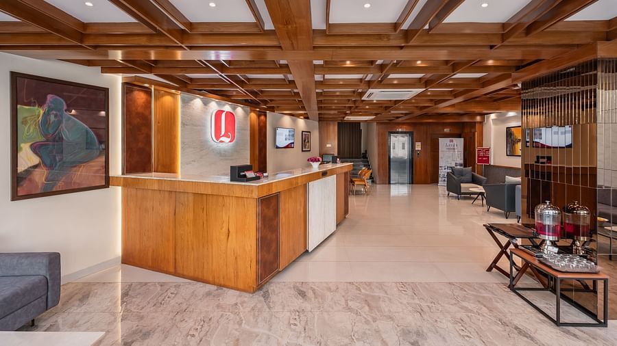 A hotel lobby features a wooden reception desk, seating areas, artwork, and a patterned floor under a beamed ceiling - Lords Eco Inn Ambaji.