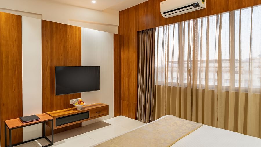 A comfortable bed is positioned in a hotel room with a mounted television and a window covered by curtains - Lords Eco Inn Ambaji.
