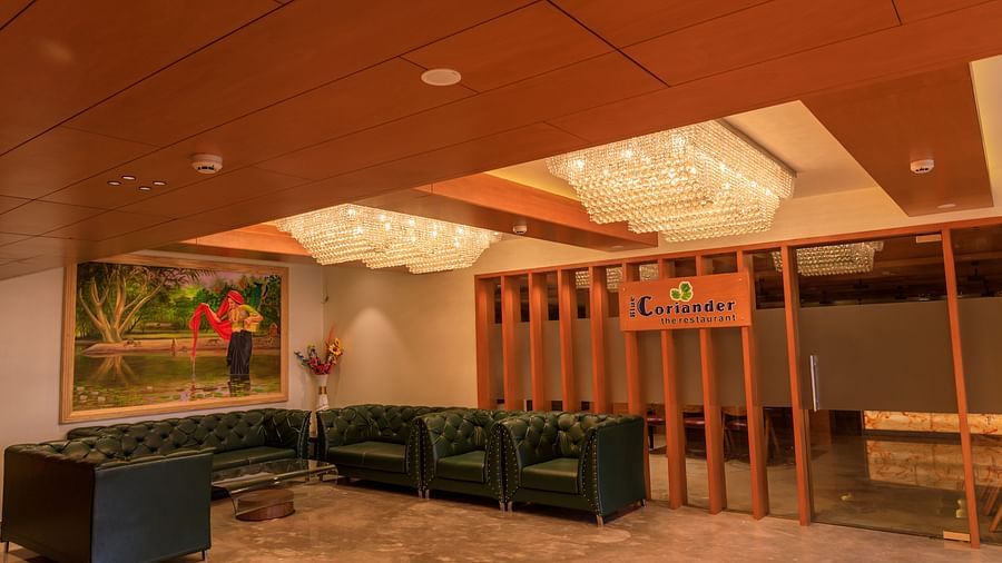 The warmly lit lobby lounge at Lords Eco Inn Apple Gate features plush dark green seating, artwork, and decorative chandeliers.