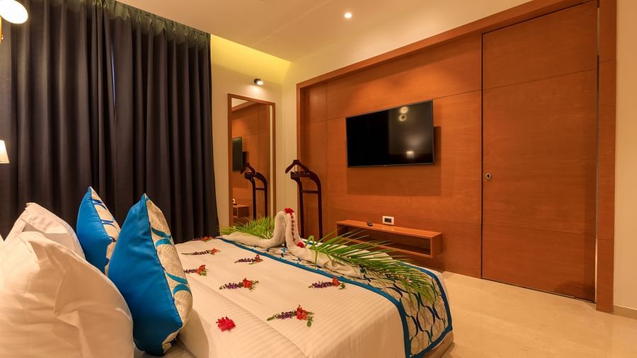 A warmly lit Executive Room at Lords Eco Inn Apple Gate features a decorated double bed, a wall-mounted TV, and dark curtains.