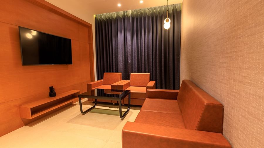 A warmly lit lounge space of Executive Room at Lords Eco Inn Apple Gate features orange sofas and armchairs, a black coffee table, and a wall-mounted TV.