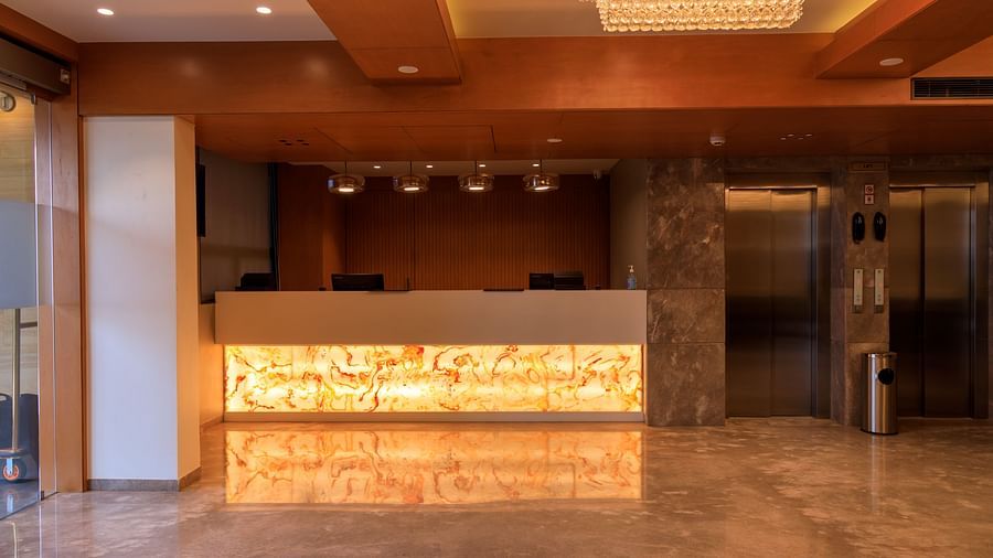 The warmly lit reception area of what appears to be Lords Eco Inn Apple Gate features a modern front desk, marble flooring, and elevators.