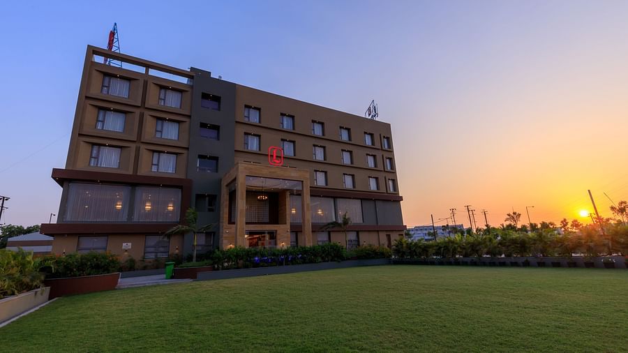 Facade of Lords Eco Inn Apple Gate hotel shown at dusk with the sun setting in the background, illuminating the modern building and green lawn.