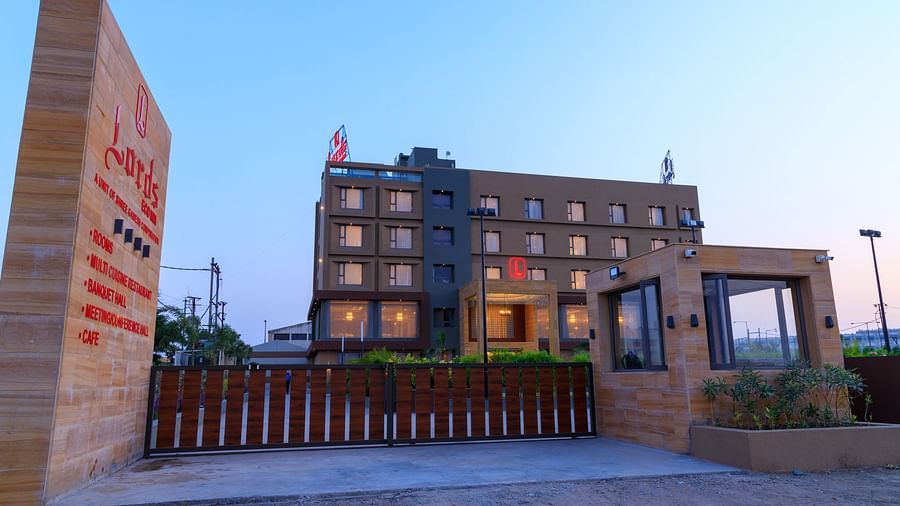 The exterior of Lords Eco Inn Apple Gate is viewed from the entrance, showing the multi-storey building, signage, and surrounding gates under a clear sky.