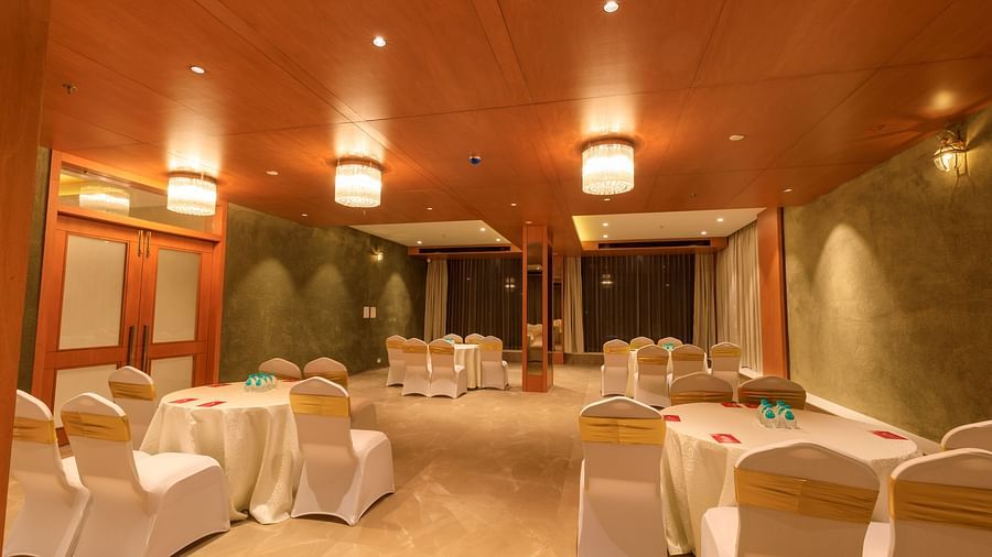 A warmly lit banquet hall at Lords Eco Inn Apple Gate is set with round tables draped in white, surrounded by chairs with gold sashes.