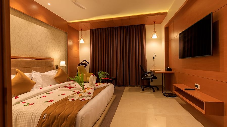 A warmly lit hotel room at Lords Eco Inn Apple Gate features a decorated double bed, a television, a desk, and brown curtains.