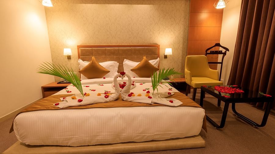 A warmly lit hotel room at Lords Eco Inn Apple Gate features a decorated double bed, bedside tables, a chair, and brown curtains.