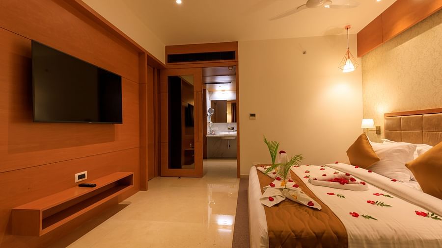A warmly lit hotel room at Lords Eco Inn Apple Gate features a decorated double bed, a wall-mounted TV, and a glimpse into the bathroom.
