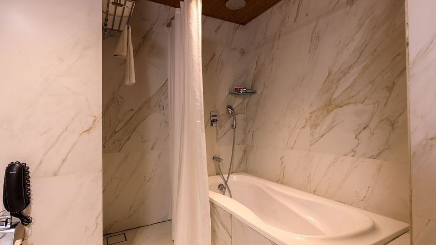 A modern bathroom at Lords Eco Inn Apple Gate features a bathtub with a shower curtain and marble-effect wall tiles.