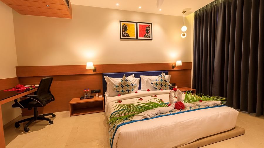 A warmly lit hotel room at Lords Eco Inn Apple Gate features a decorated double bed, bedside tables, a desk with a chair, and dark curtains.
