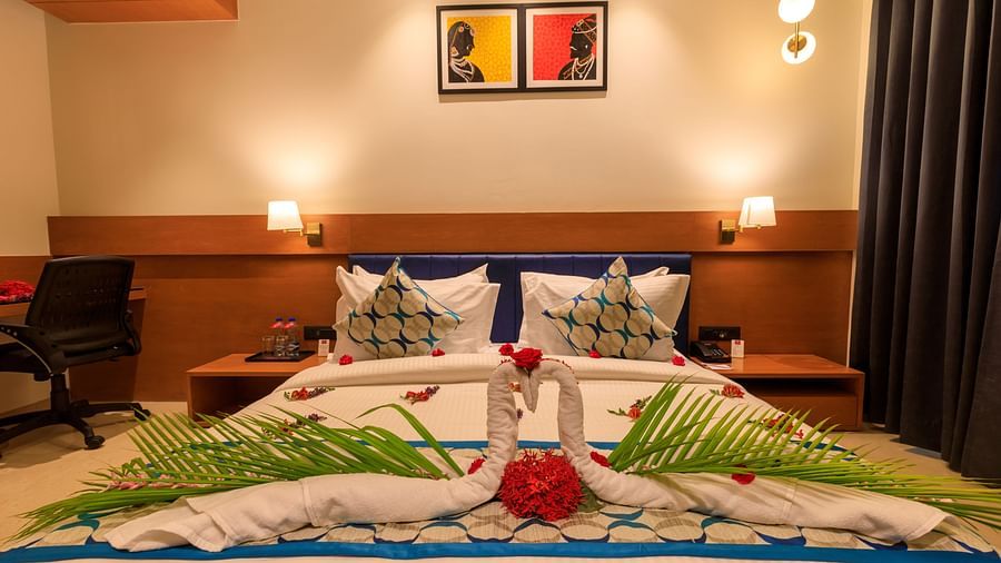 A decorated double bed in a warmly lit room at Lords Eco Inn Apple Gate, featuring towel swans and floral arrangements.