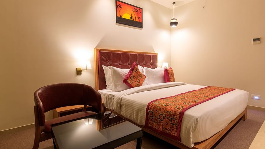 A warmly lit hotel room at Lords Eco Inn Apple Gate features a double bed with patterned accents, a chair and a small table.