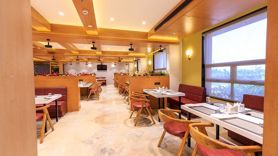 The brightly lit restaurant at Lords Eco Inn Apple Gate features set tables, red chairs, wooden accents, and natural light from large windows.