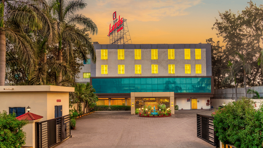  The exterior of a Lords Eco Inn hotel building with a green facade, an outdoor area, and flags on the roof.