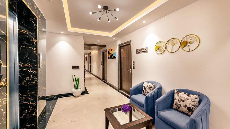 Well-lit hotel corridor with blue armchairs, a glass coffee table, modern ceiling lights, and an elevator - Lords Eco Inn Dehradun.