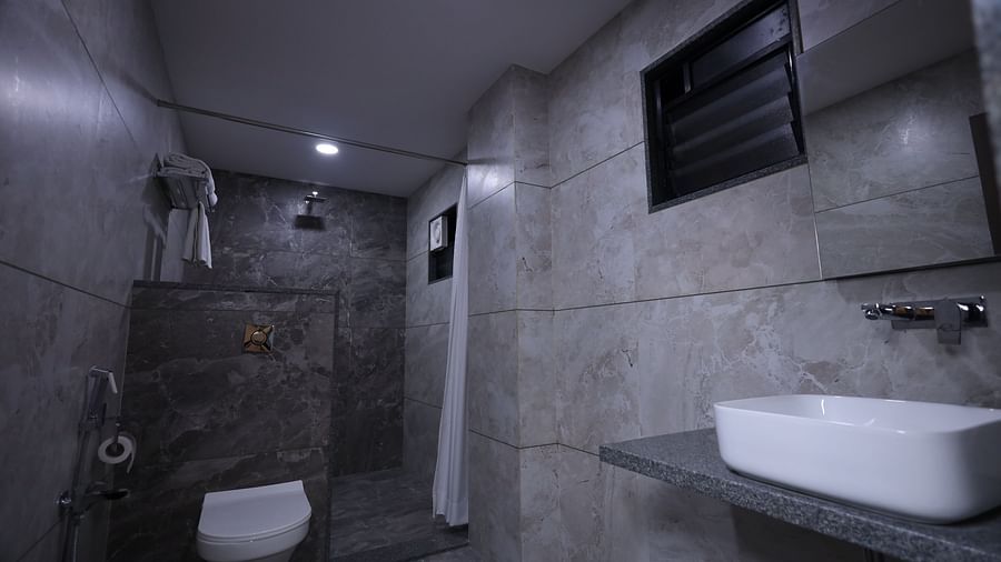 A bathroom features a toilet, a shower with a curtain, a sink on a counter, and towels hanging nearby - Lords Eco Inn Navsari.