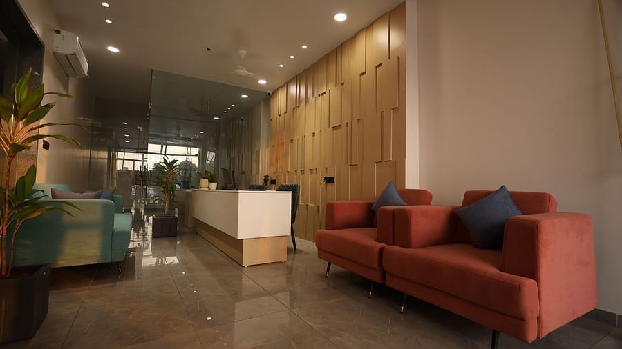 The image shows a reception or waiting area with sofas, a front desk, and a potted plant - Lords Eco Inn Navsari.