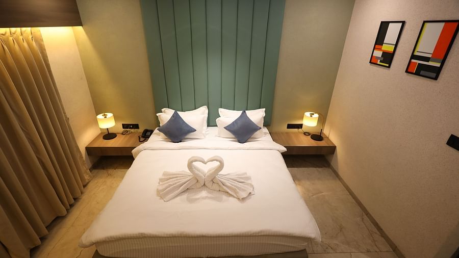 A hotel room in Navsari presents a bed with swan-shaped folded towels, flanked by nightstands and lamps - Lords Eco Inn Navsari.