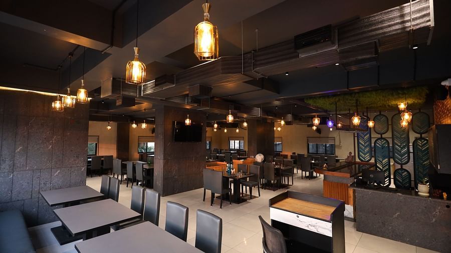 The image shows a restaurant interior with tables, chairs, booth seating, a service counter, and warm pendant lighting - Lords Eco Inn Navsari.
