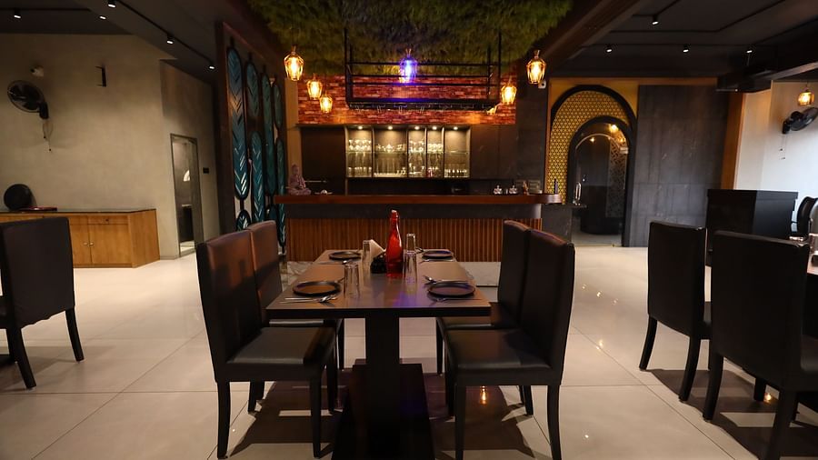 The image shows a restaurant dining area with set tables and chairs, a bar in the background, and warm lighting - Lords Eco Inn Navsari.