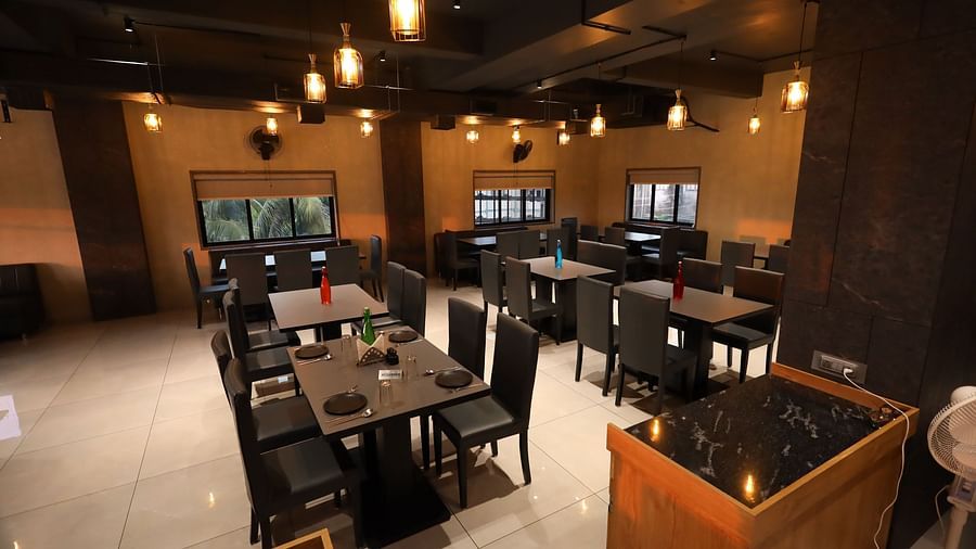 The image depicts a restaurant interior with set tables and chairs under warm, hanging lights - Lords Eco Inn Navsari.