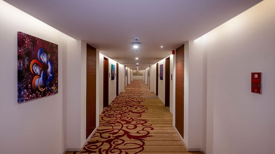 Hotel hallway with patterned carpet, wall art, and lighting leading to guest rooms - Lords Eco Inn Shapar Rajkot