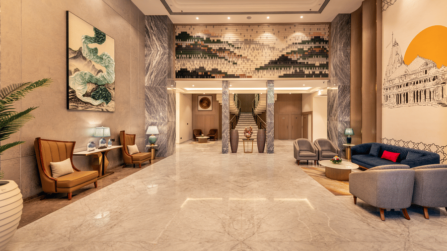 Lobby with elegant mural wall art, wooden seating chairs, and a plush blue sofa at Lords Inn Somnath, offering a welcoming ambiance.