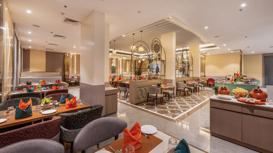 Restaurant buffet counter with a chef preparing dishes and vibrant geometric flooring at Lords Inn Somnath, offering fresh cuisine.