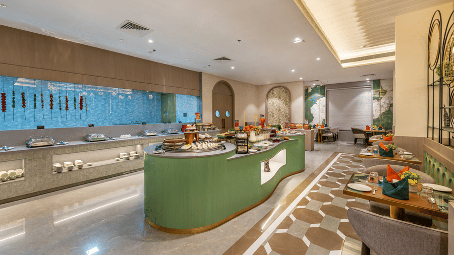 Restaurant dining area with wooden tables, colorful napkins, and a nearby buffet counter at Lords Inn Somnath, welcoming guests.