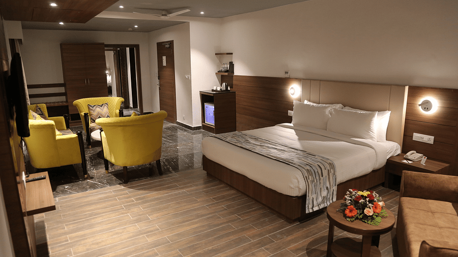 A spacious hotel room features a neatly made bed, a seating area with yellow armchairs, and modern decor under soft lighting.