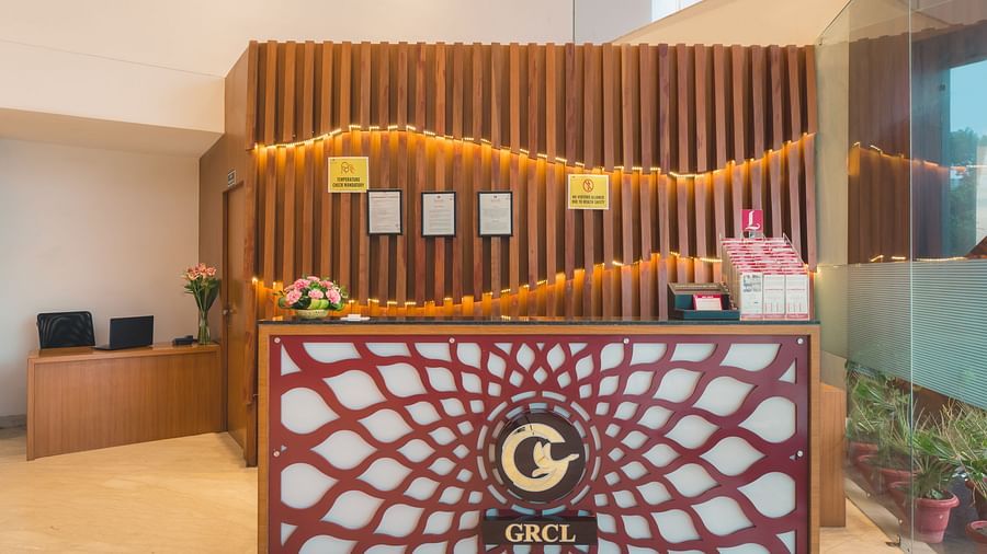 The reception area of Lords Inn Udaipur features a decorative front desk with a central logo, set against a wooden slat wall with framed displays.