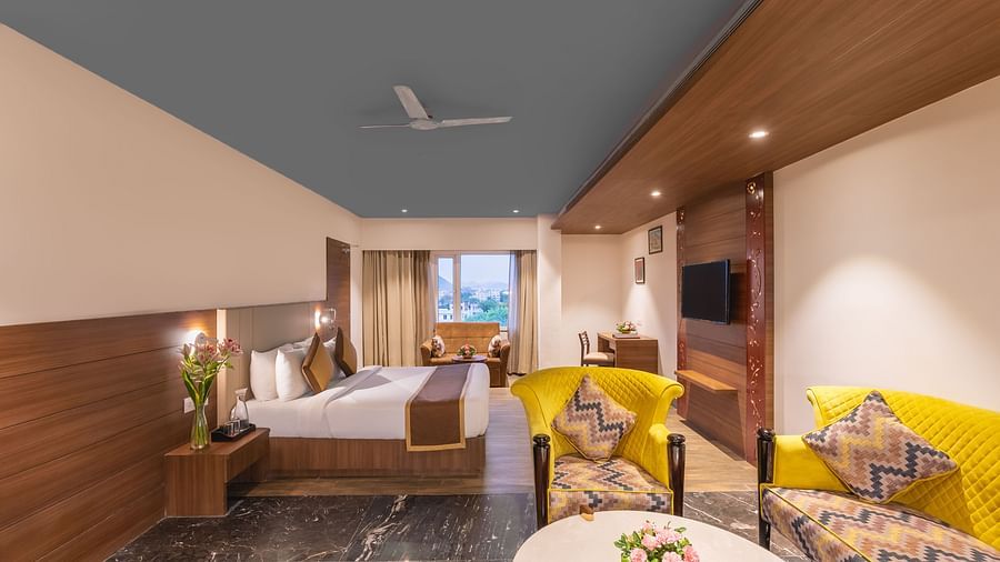 A spacious suite at Lords Inn Udaipur features a comfortable bed, bright yellow seating around a table with flowers, and modern decor.
