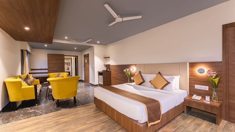 A spacious hotel room at Lords Inn Udaipur includes a comfortable bed, a seating area with bright yellow armchairs, and modern amenities.