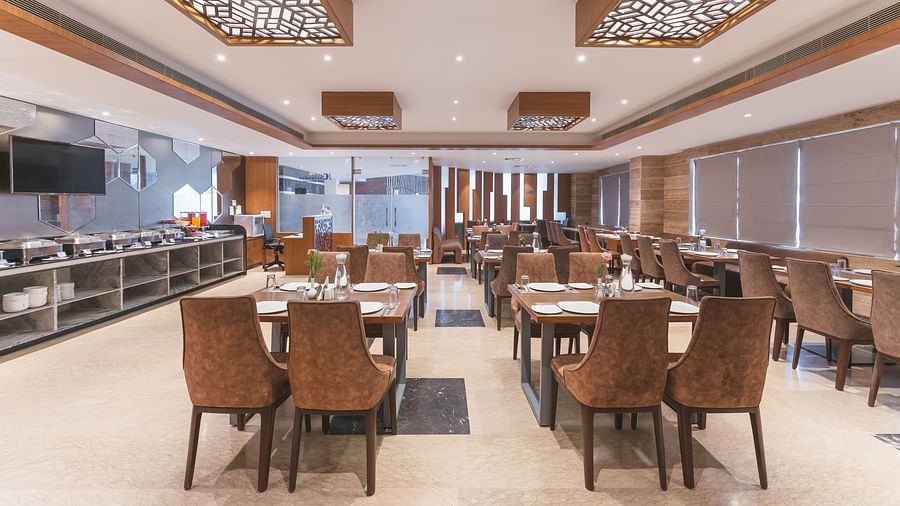 The spacious dining area at Lords Inn Udaipur is furnished with numerous tables and chairs, and features a buffet service along one wall.