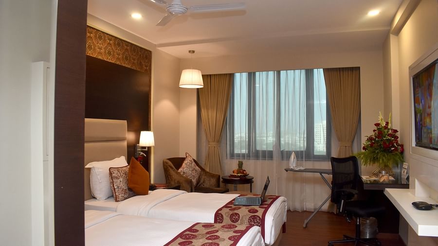 A hotel room with a bed, desk, and chair near a window at Lords Plaza Surat.