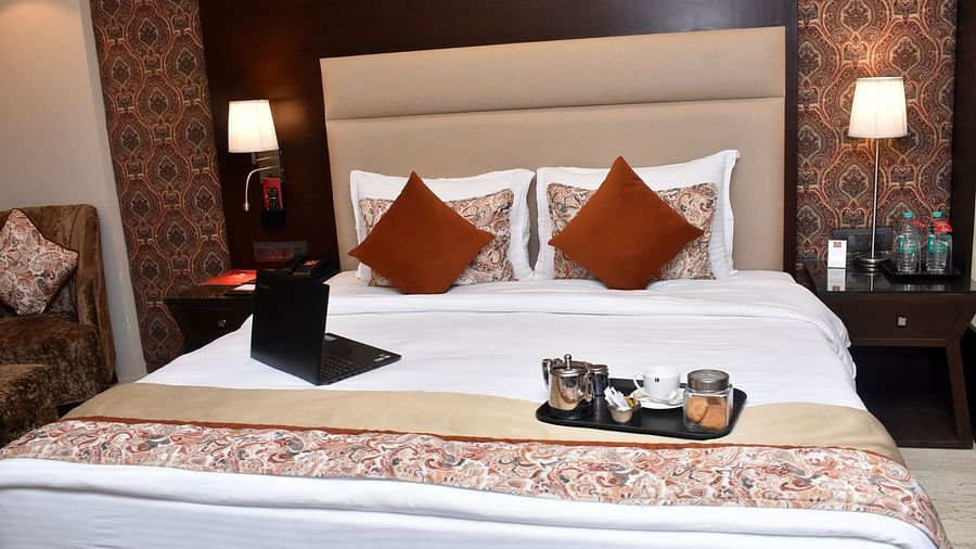 A neatly made bed with decorative pillows and a dark throw in a room at Lords Plaza Surat.