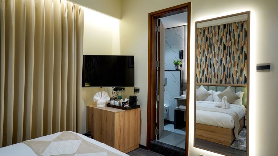 A wall-mounted television alongside a door leading to the bathroom and a full length mirror in the Deluxe Room at M2 Square by Monday Premium.