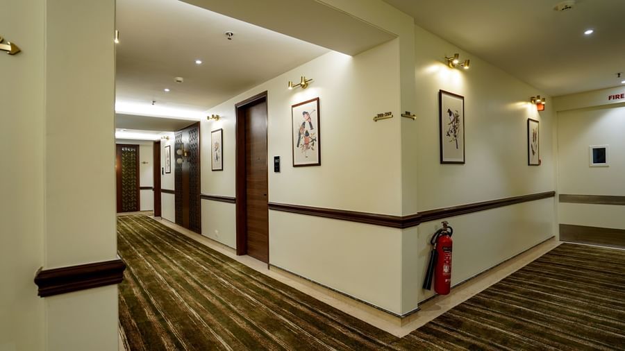 Corner of a corridor with carpeted flooring along with a fire extinguisher mounted on the wall at M2 Square by Monday Premium.