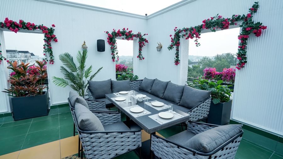 A wide angle shot of a dining table with a capacity of 6 people featuring a white coloured wall behind it at the Sky Roof during the day at M2 Square by Monday Premium.