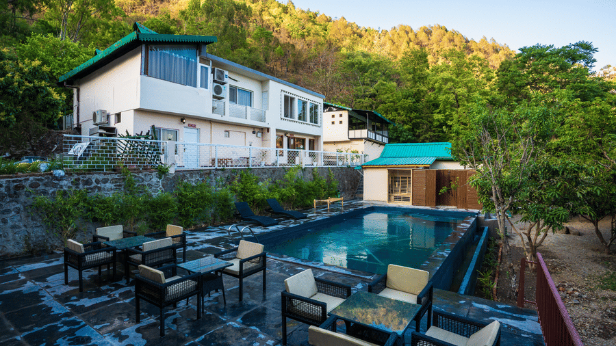 Outdoor swimming pool area surrounded by lush greenery and guest rooms at Maati Resort By The Lake Hill, Jeolikote.