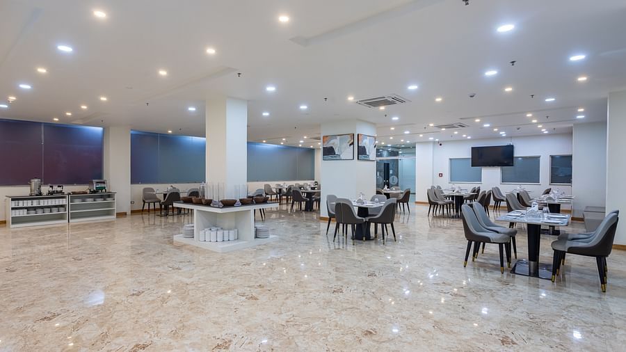 Corner view of the Blue Coriander Restaurant at Mandala Norling Lords Prime in Kathmandu with various seating arrangements, neatly placed cutlery and bright overhead lighting.