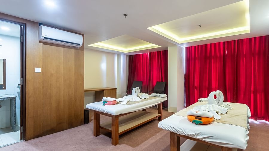 Two spa tables placed in a room with carpeted flooring, curtained windows, a chair and a table at Mandala Norling Lords Prime in Kathmandu.