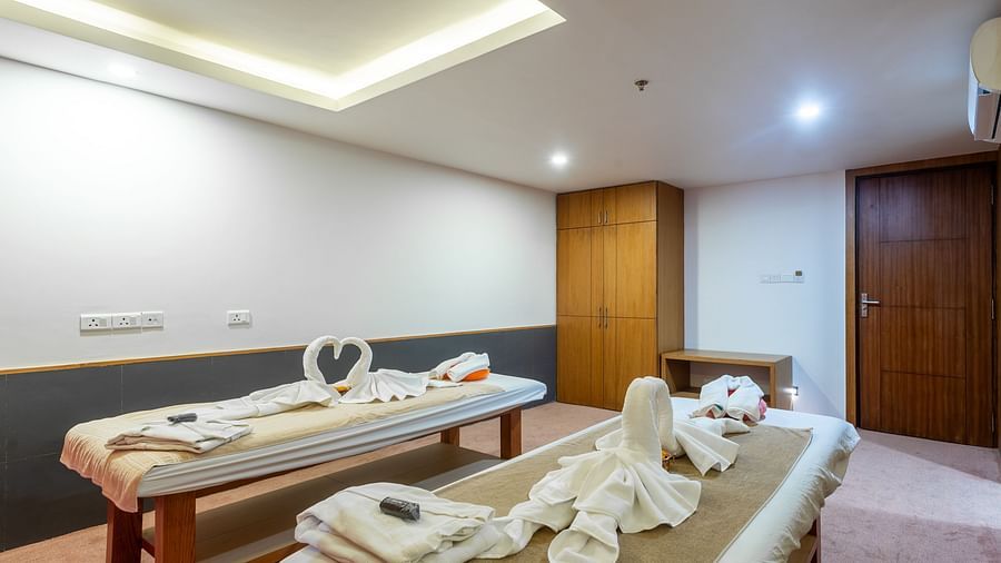 Two spa tables placed in a room with carpeted flooring, curtained windows, a chair and a table at Mandala Norling Lords Prime in Kathmandu.