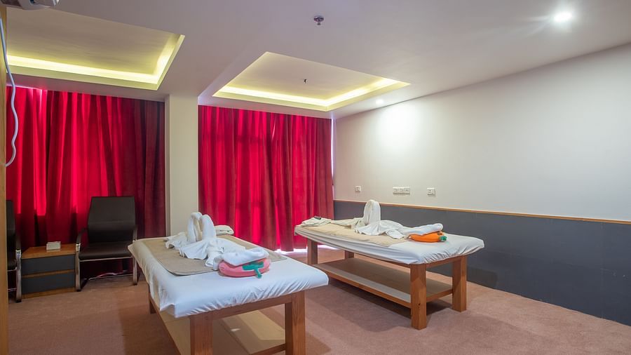 Two spa tables placed in a room with carpeted flooring, curtained windows, a chair and a table at Mandala Norling Lords Prime in Kathmandu.