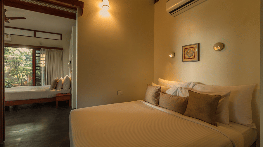 Villa Wuwei in Mango Hill Auroville, Pondicherry featuring a bed is placed against a wall with a doorway leading to another room and a unit mounted above.